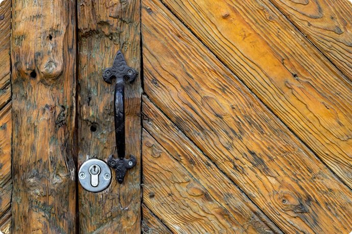 Detalle de puerta de madera histórica en el casco antiguo de Sabadell con instalación de cilindro de alta seguridad grado 4.