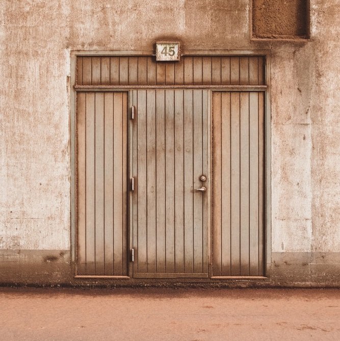Puerta antigua en Sabadell que presenta signos severos de fatiga mecánica y oxidación en su sistema de cierre exterior, urge sustituir cerradura o cambio de puerta.